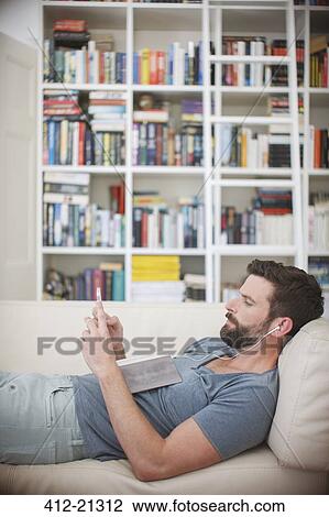 Stock Image - Man listening to music on sofa. Fotosearch