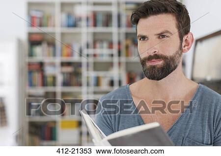 Stock Image - Man reading book in living room. Fotosearch