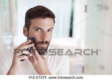 Stock Photography - Man trimming beard in bathroom mirror. Fotosearch
