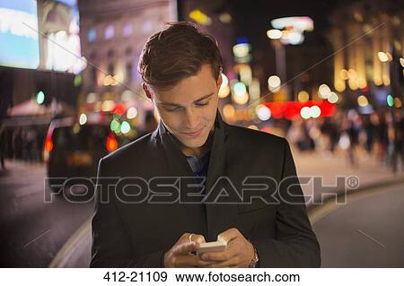 Stock Photo - Man using cell phone on city street at night. Fotosearch