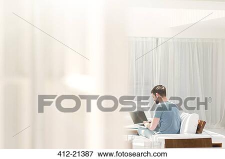 Man using laptop on sofa in modern living room View Large Photo Image Stock Photo - Man using laptop on sofa in modern living room. Fotosearch
