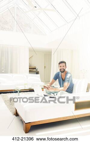 Man using laptop on sofa in modern living room View Large Photo Image Stock Photograph - Man using laptop on sofa in modern living room. Fotosearch