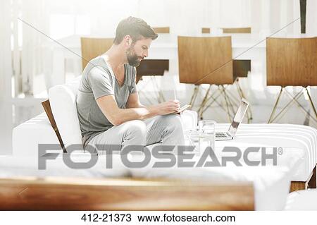 Man writing notes at laptop on sofa in modern living room View Large Photo Image Stock Image - Man writing notes at laptop on sofa in modern living room. Fotosearch