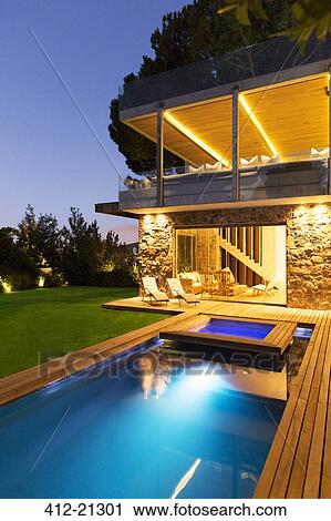 Stock Image - Modern house overlooking illuminated swimming pool at night. Fotosearch