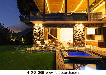 Stock Photograph - Modern house overlooking illuminated swimming pool at night. Fotosearch