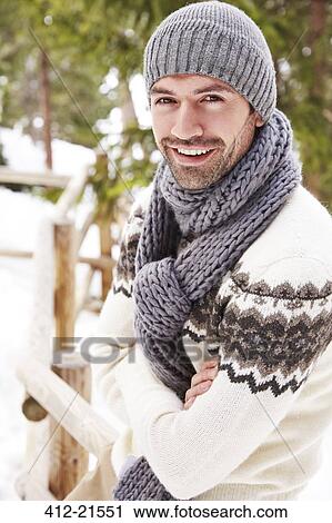 Stock Image - Smiling man sitting on snowy fence . Fotosearch