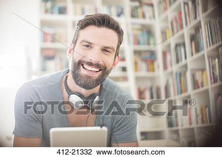 Stock Image - Smiling man using digital tablet in living room. Fotosearch