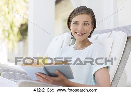 Stock Photography - Smiling woman reading book in lawn chair. Fotosearch