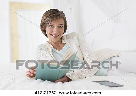 Smiling woman reading book on bed View Large Photo Image Stock Image - Smiling woman reading book on bed. Fotosearch