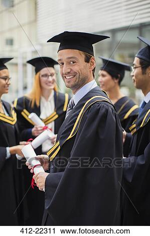 Stock Image - Student in cap and gown standing with friends. Fotosearch