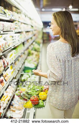 Woman carrying full shopping basket in grocery store View Large Photo Image Stock Image - Woman carrying full shopping basket in grocery store. Fotosearch