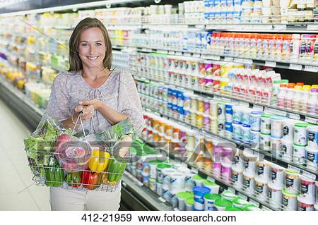Woman carrying full shopping basket in grocery store View Large Photo Image Stock Photo - Woman carrying full shopping basket in grocery store. Fotosearch