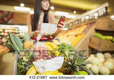 Stock Photo - Woman checking shopping list in grocery store. Fotosearch