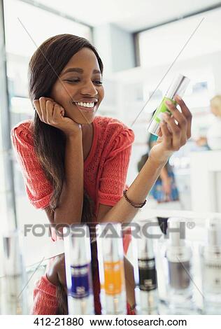 Stock Image - Woman examining skincare product in drugstore. Fotosearch
