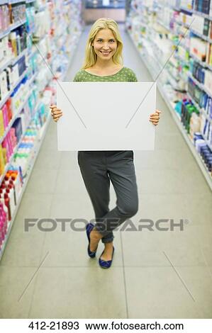 Stock Image - Woman holding blank card in grocery store aisle. Fotosearch