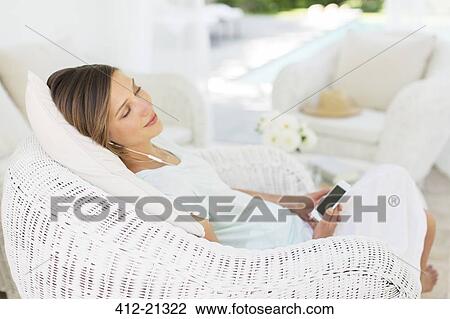 Woman listening to music in wicker chair View Large Photo Image Stock Image - Woman listening to music in wicker chair. Fotosearch