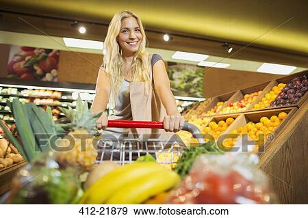 Stock Photo - Woman pushing full shopping cart in grocery store. Fotosearch