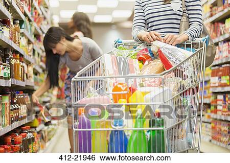 Stock Photograph - Woman pushing full shopping cart in grocery store. Fotosearch