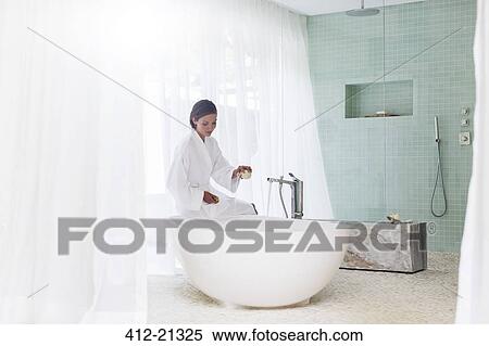 Stock Photography - Woman running bath in modern bathroom. Fotosearch