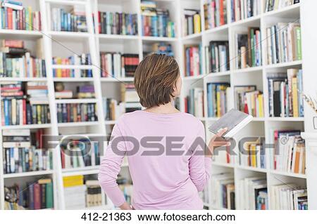 Stock Image - Woman selecting book from library. Fotosearch