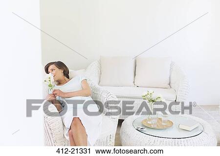 Woman smelling flowers in wicker chair in living room View Large Photo Image Stock Image - Woman smelling flowers in wicker chair in living room. Fotosearch