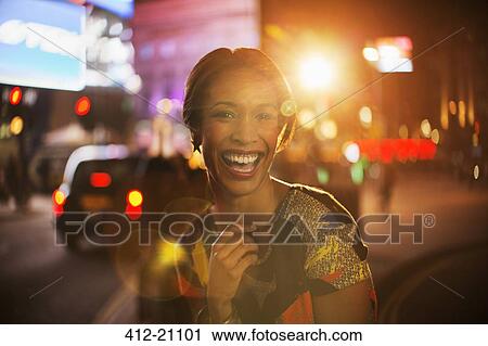 Stock Image - Woman smiling on city street at night . Fotosearch