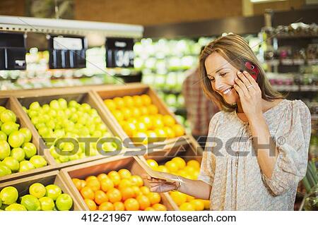 Woman talking on cell phone while shopping in grocery store View Large Photo Image Stock Photo - Woman talking on cell phone while shopping in grocery store. Fotosearch
