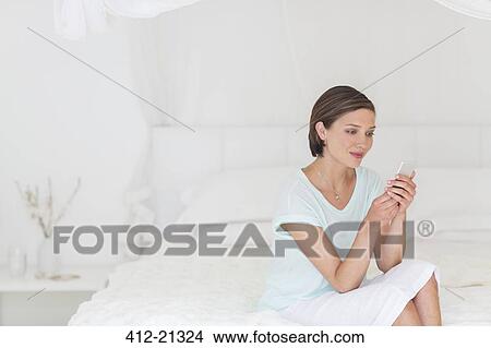 Picture - Woman using cell phone on bed. Fotosearch