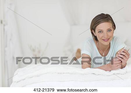 Stock Photo - Woman using cell phone on bed. Fotosearch