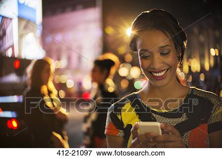 Woman using cell phone on city street at night View Large Photo Image Stock Photo - Woman using cell phone on city street at night. Fotosearch