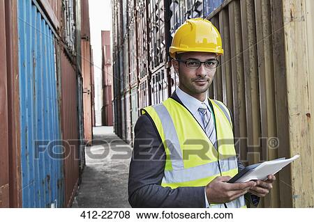 Businessman holding digital tablet between cargo containers View Large Photo Image Stock Photo - Businessman holding digital tablet between cargo containers. Fotosearch