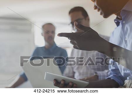 Stock Photography - Businessmen using digital tablet and laptop in office. Fotosearch