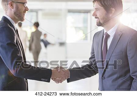 Businessmen wearing suits shaking hands in office, colleagues in background View Large Photo Image Stock Image - Businessmen wearing suits shaking hands in office, colleagues in background. Fotosearch