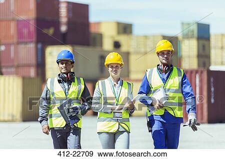 Stock Photo - Businesswoman and workers walking near cargo containers. Fotosearch