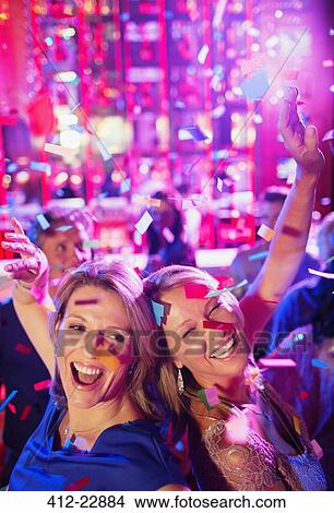 Picture - Confetti falling on two women dancing back to back in nightclub. Fotosearch