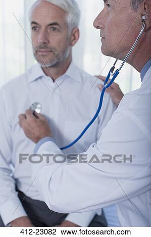 Stock Image - Doctor examining patient with stethoscope in office. Fotosearch