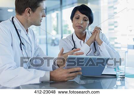 Doctors discussing patient's treatment at desk, using digital tablet View Large Photo Image Stock Photo - Doctors discussing patient's treatment at desk, using digital tablet. Fotosearch