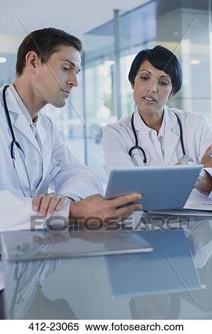 Doctors discussing patient's treatment at desk, using digital tablet View Large Photo Image Stock Photography - Doctors discussing patient's treatment at desk, using digital tablet. Fotosearch