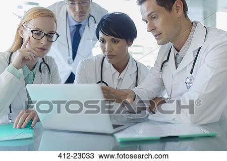 Stock Image - Doctors using laptop and discussing patient's treatment. Fotosearch