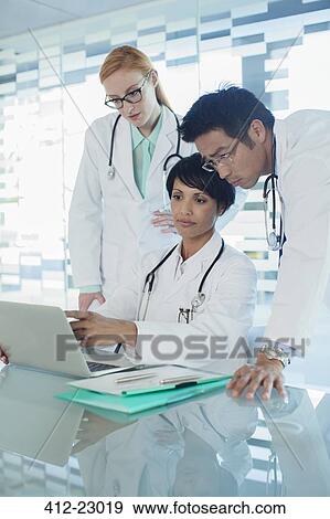 Stock Photo - Doctors using laptop and discussing patient's treatment. Fotosearch