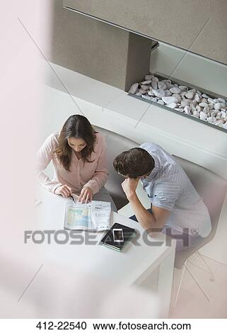 Stock Image - Elevated view of couple reading newspaper in their dining room. Fotosearch