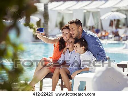 Stock Photograph - Family with two children taking selfie by resort swimming pool. Fotosearch