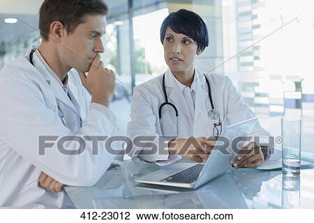 Stock Image - Female and male doctor using laptop in hospital office. Fotosearch
