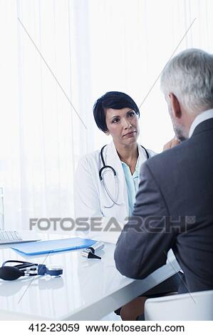 Female doctor and man sitting at desk in office View Large Photo Image Stock Photo - Female doctor and man sitting at desk in office. Fotosearch