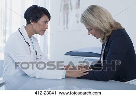 Female doctor consoling sad woman at desk in office View Large Photo Image Stock Image - Female doctor consoling sad woman at desk in office. Fotosearch