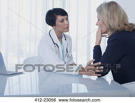 Female doctor consoling sad woman at desk in office View Large Photo Image Stock Photograph - Female doctor consoling sad woman at desk in office. Fotosearch