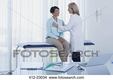 Female doctor examining her patient with stethoscope in office, desk with laptop in foreground View Large Photo Image Picture - Female doctor examining her patient with stethoscope in office, desk with laptop in foreground. Fotosearch