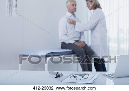 Female doctor examining patient in office, laptop, file, glasses and otoscope on desk in foreground View Large Photo Image Stock Image - Female doctor examining patient in office, laptop, file, glasses and otoscope on desk in foreground. Fotosearch