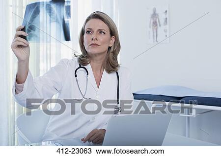 Female doctor looking at x-ray at desk with laptop in office View Large Photo Image Stock Image - Female doctor looking at x-ray at desk with laptop in office. Fotosearch