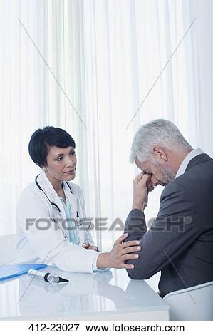 Female doctor sitting at desk and consoling sad patient View Large Photo Image Stock Photo - Female doctor sitting at desk and consoling sad patient. Fotosearch